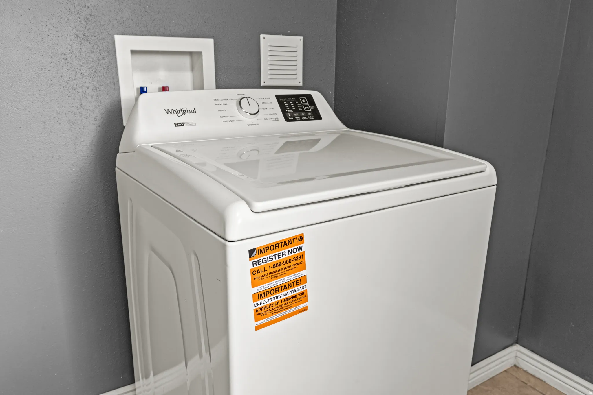 White top-loading washing machine with digital controls, featuring a water hookup box and an exhaust vent