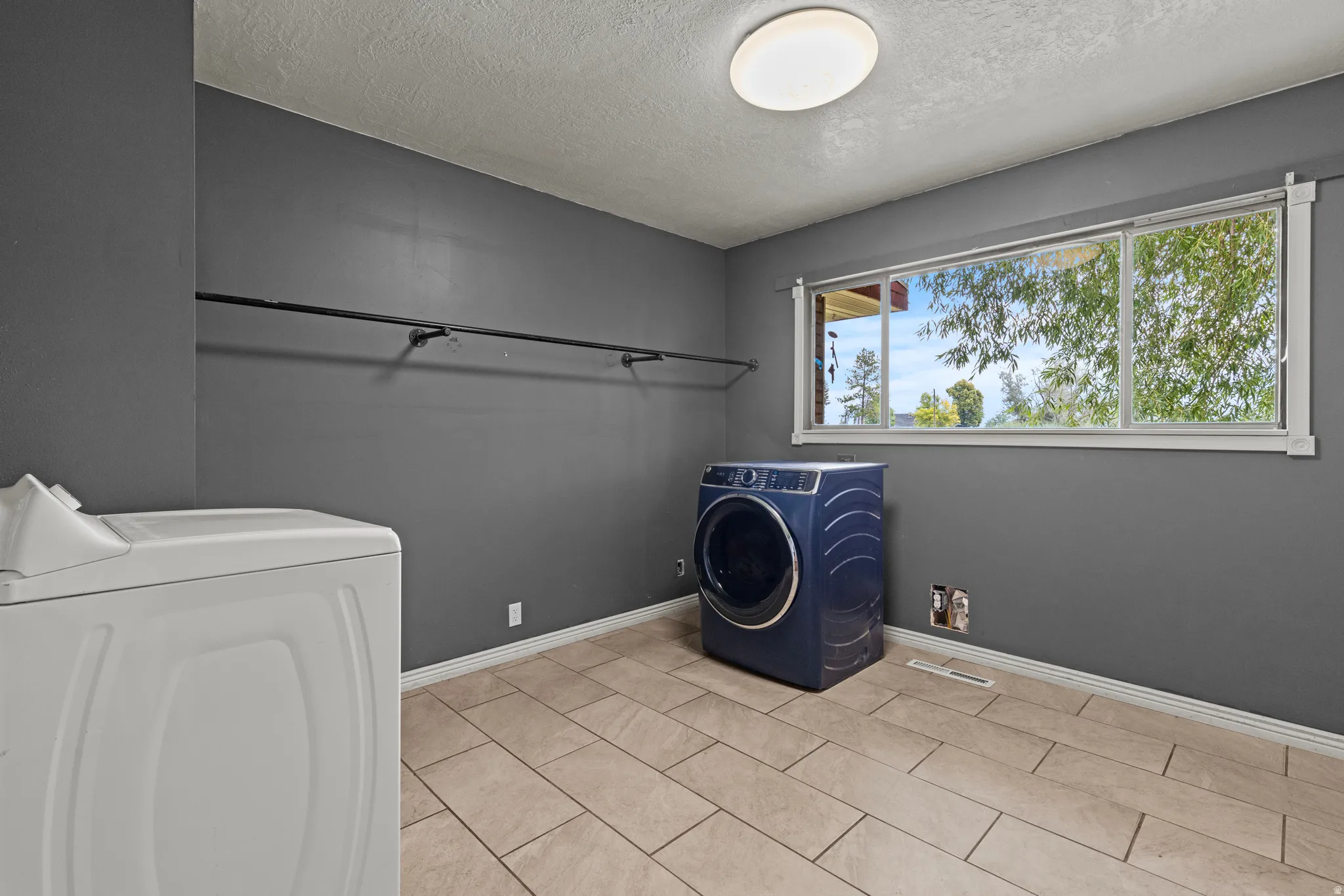 Utility room featuring tile flooring, a large window, a ceiling light fixture, and a built-in hanging rod