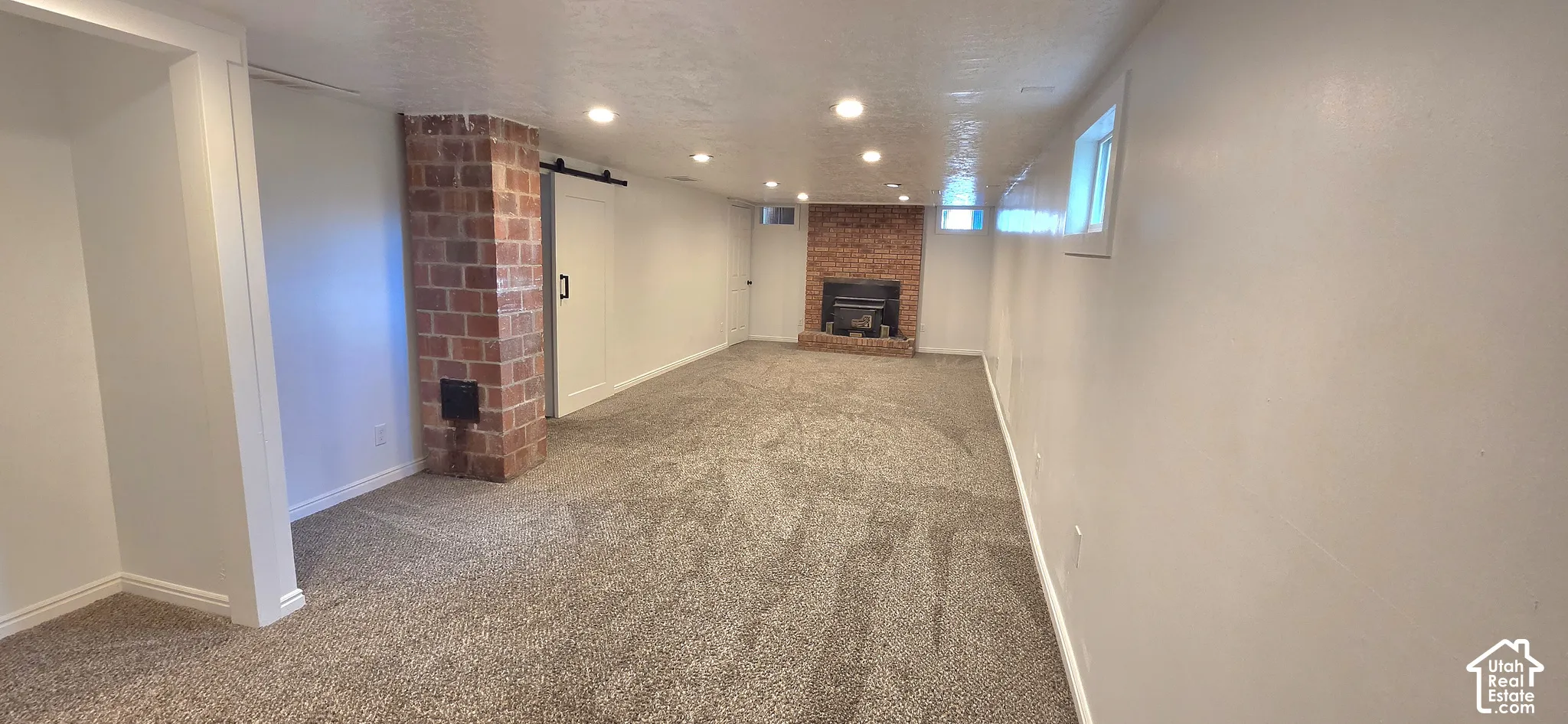 Spacious room featuring neutral carpeting, recessed lighting, and a brick fireplace