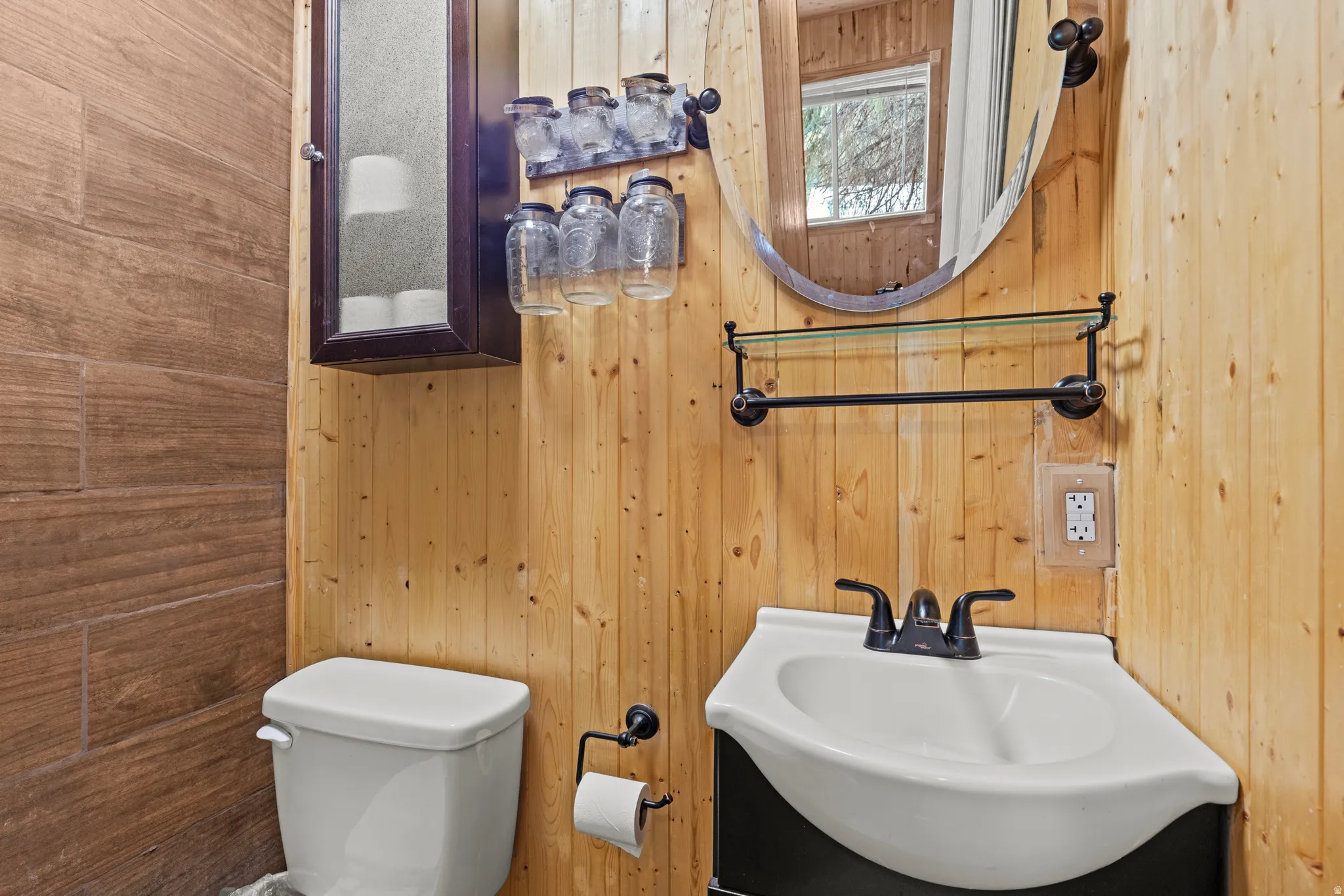 Corner pedestal sink with black hardware, flanked by natural wood plank walls