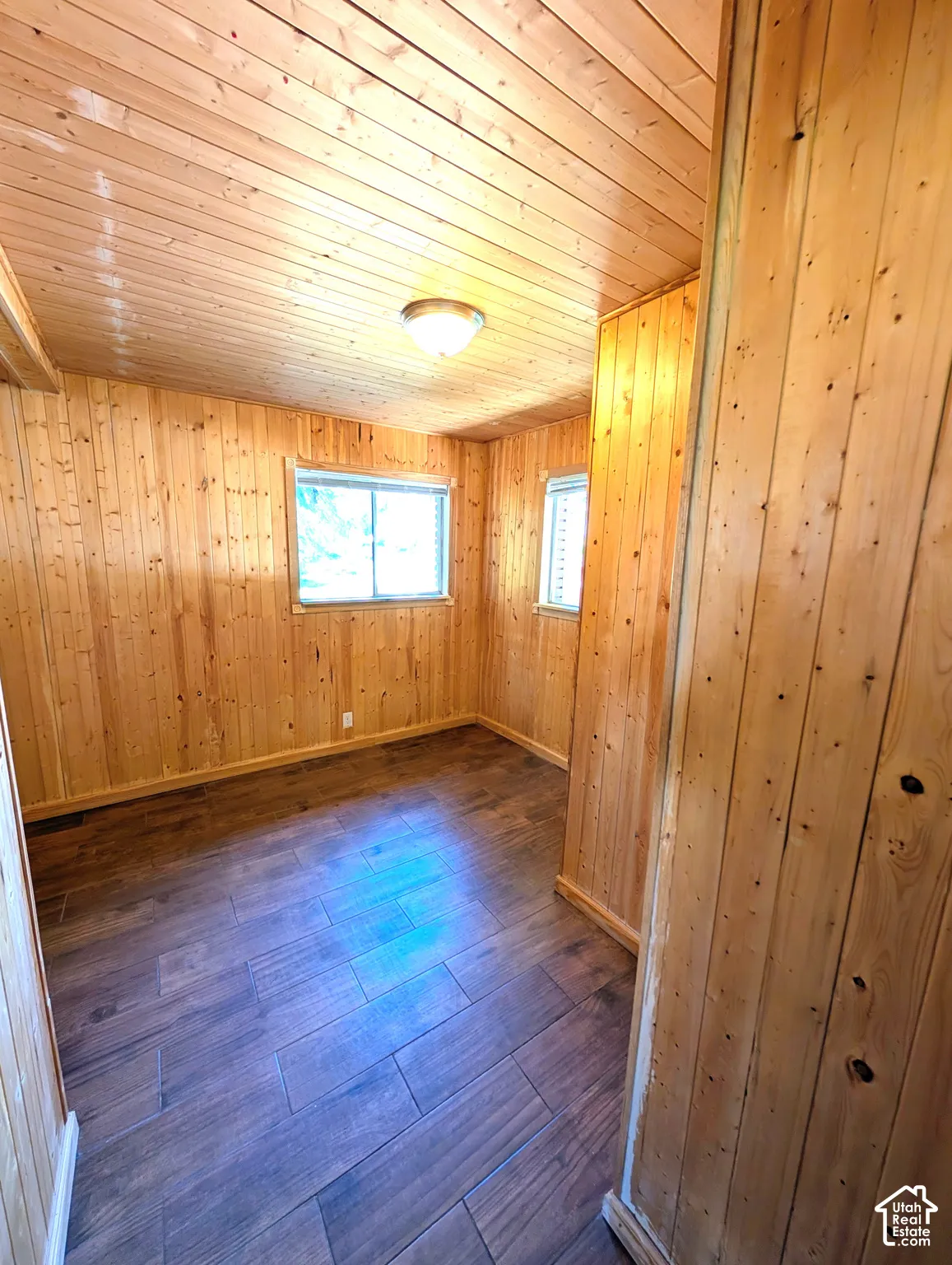 Interior room featuring wood-finish walls and ceiling, dark wood-finish flooring laid in a linear pattern, and natural light from dual windows
