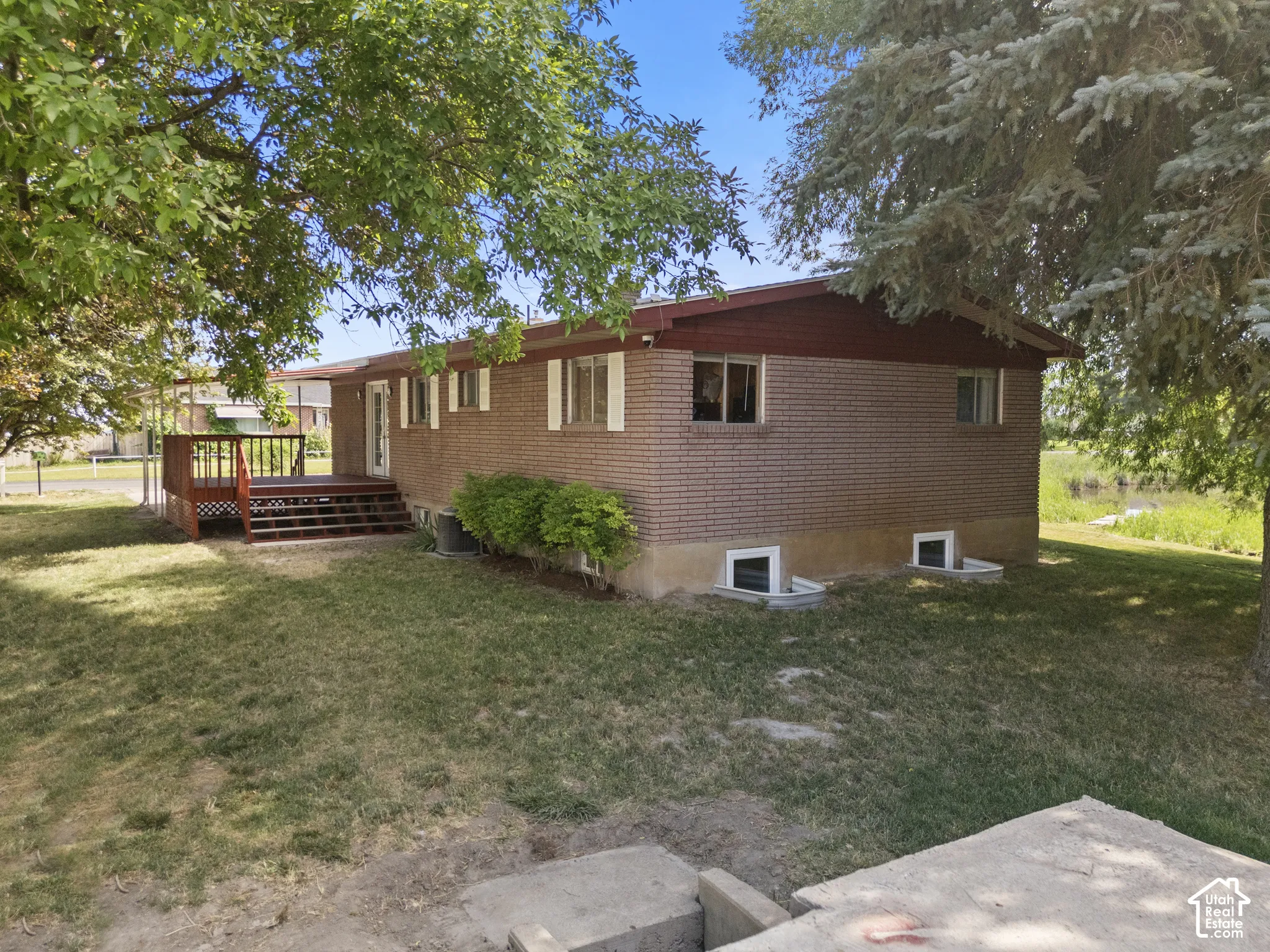 Brick exterior featuring a wood deck with lattice railing, multiple windows, and mature trees providing shade