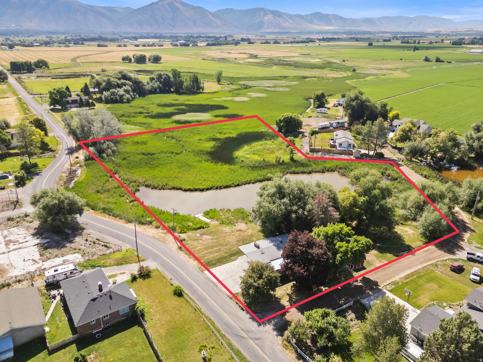 Expansive parcel featuring a natural pond, surrounding wetlands, mature trees, and a distant mountain backdrop