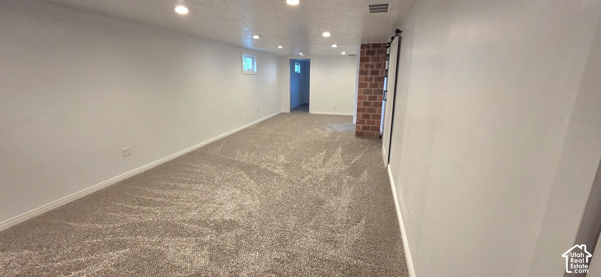 Recessed lighting illuminates neutral carpeting and a exposed brick