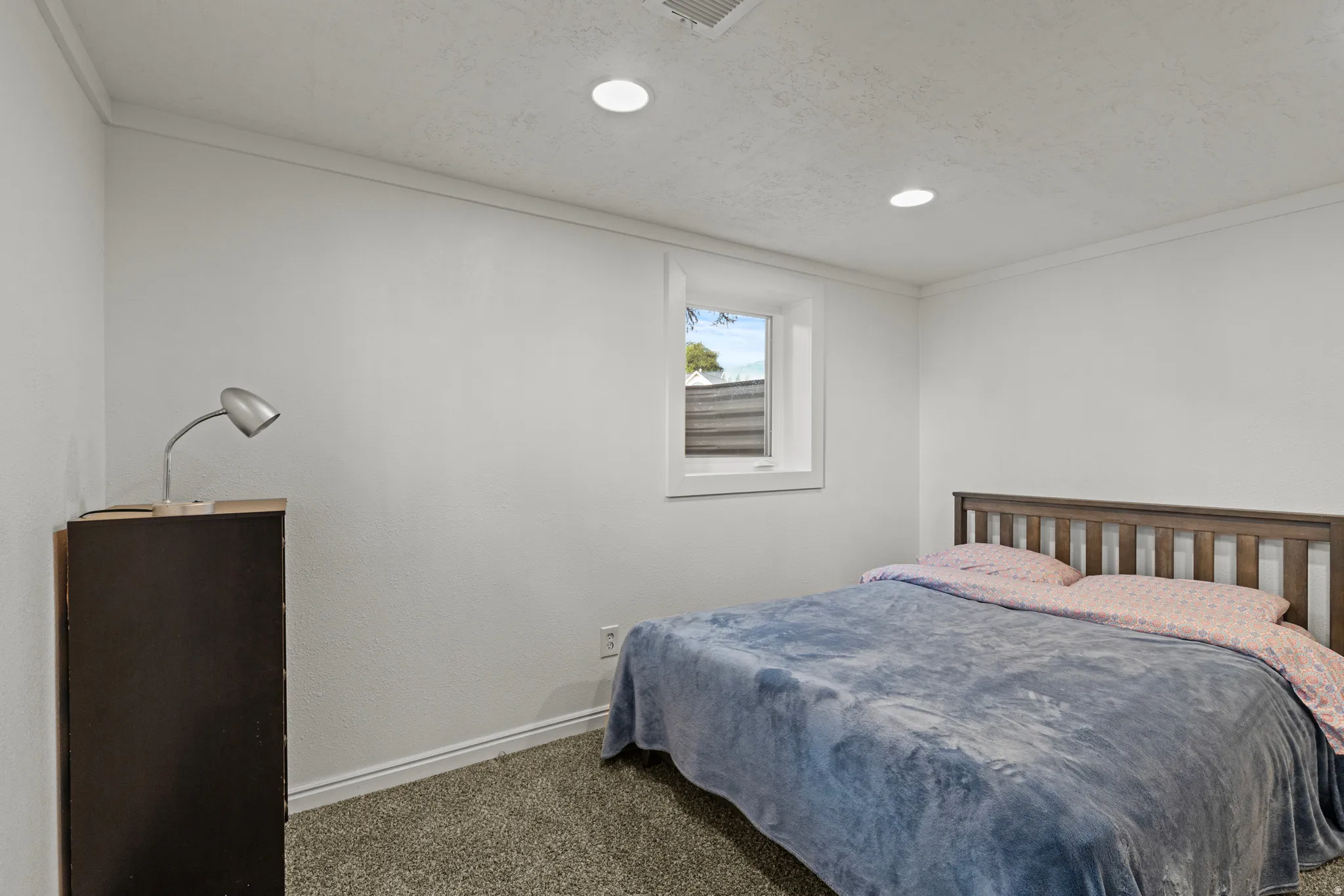 Recessed lighting illuminates a room featuring a window with white trim, and white walls.