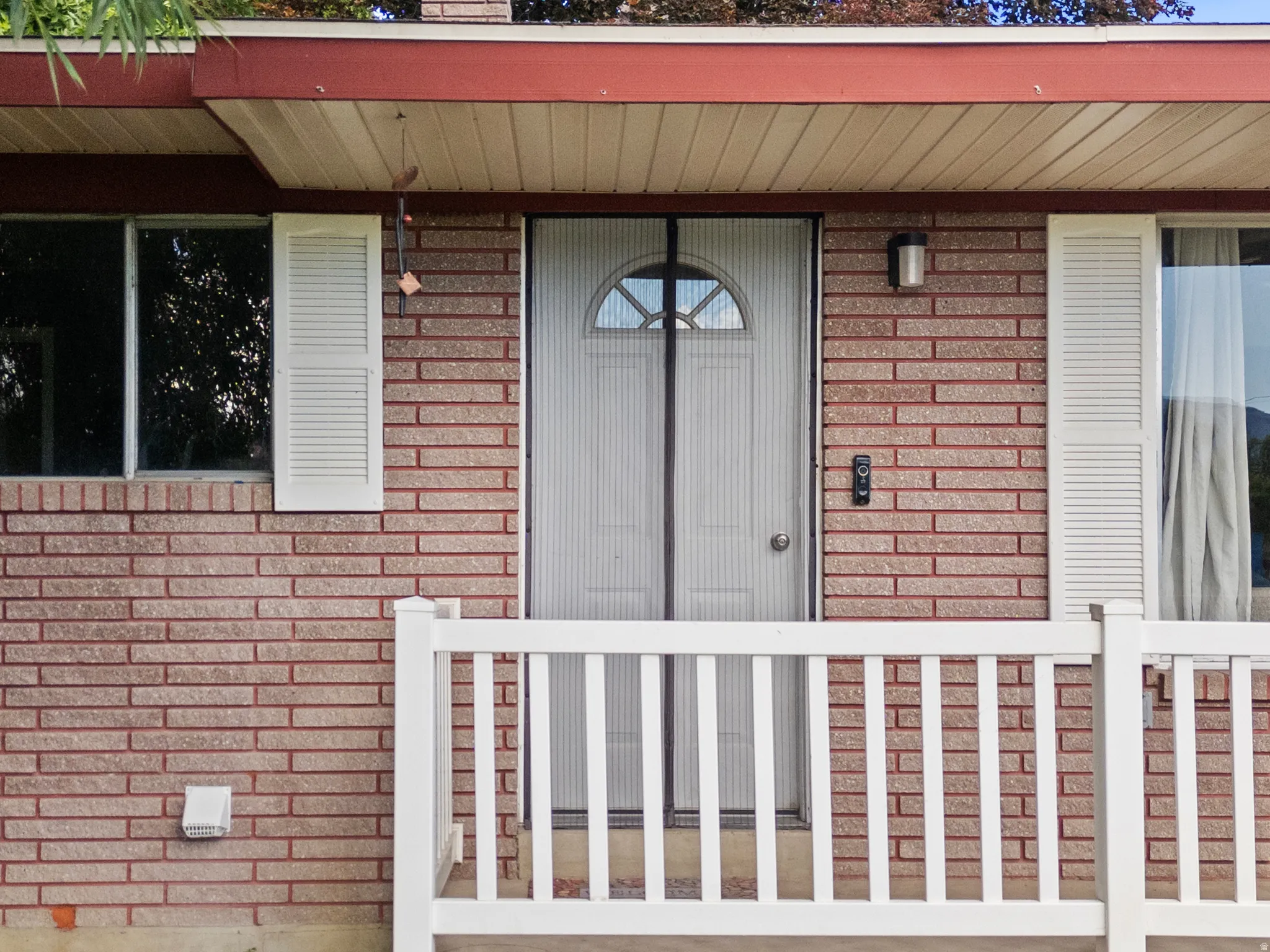 Brick facade featuring a white railing, white louvered shutters, and a white front door with an arched window
