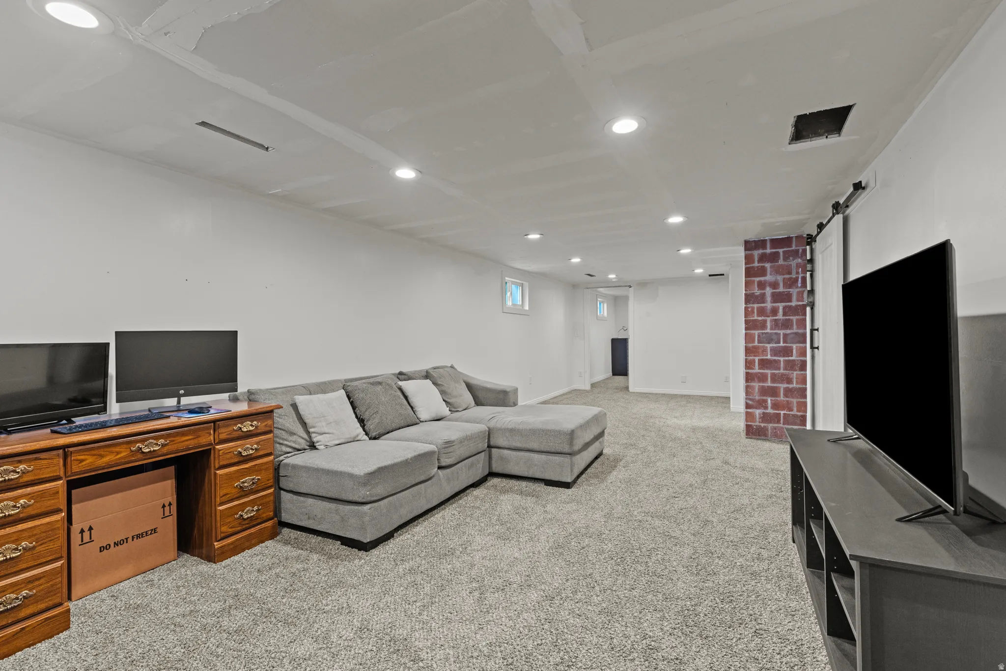 Spacious lower-level area featuring recessed lighting, a barn door, a brick chimney, and gray carpet flooring