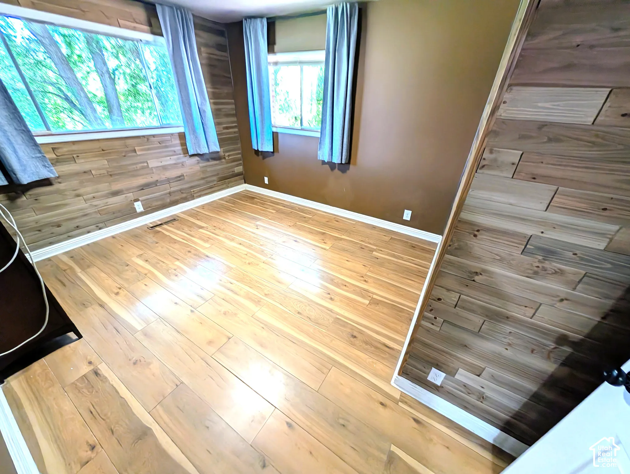 Wood-finish flooring with white trim, multiple windows, and partial wood walls