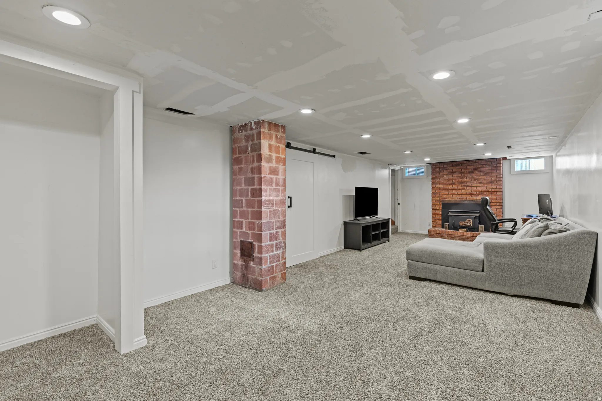 Spacious lower level featuring light gray carpeting, a prominent brick-chimney, recessed lighting, and a brick fireplace.