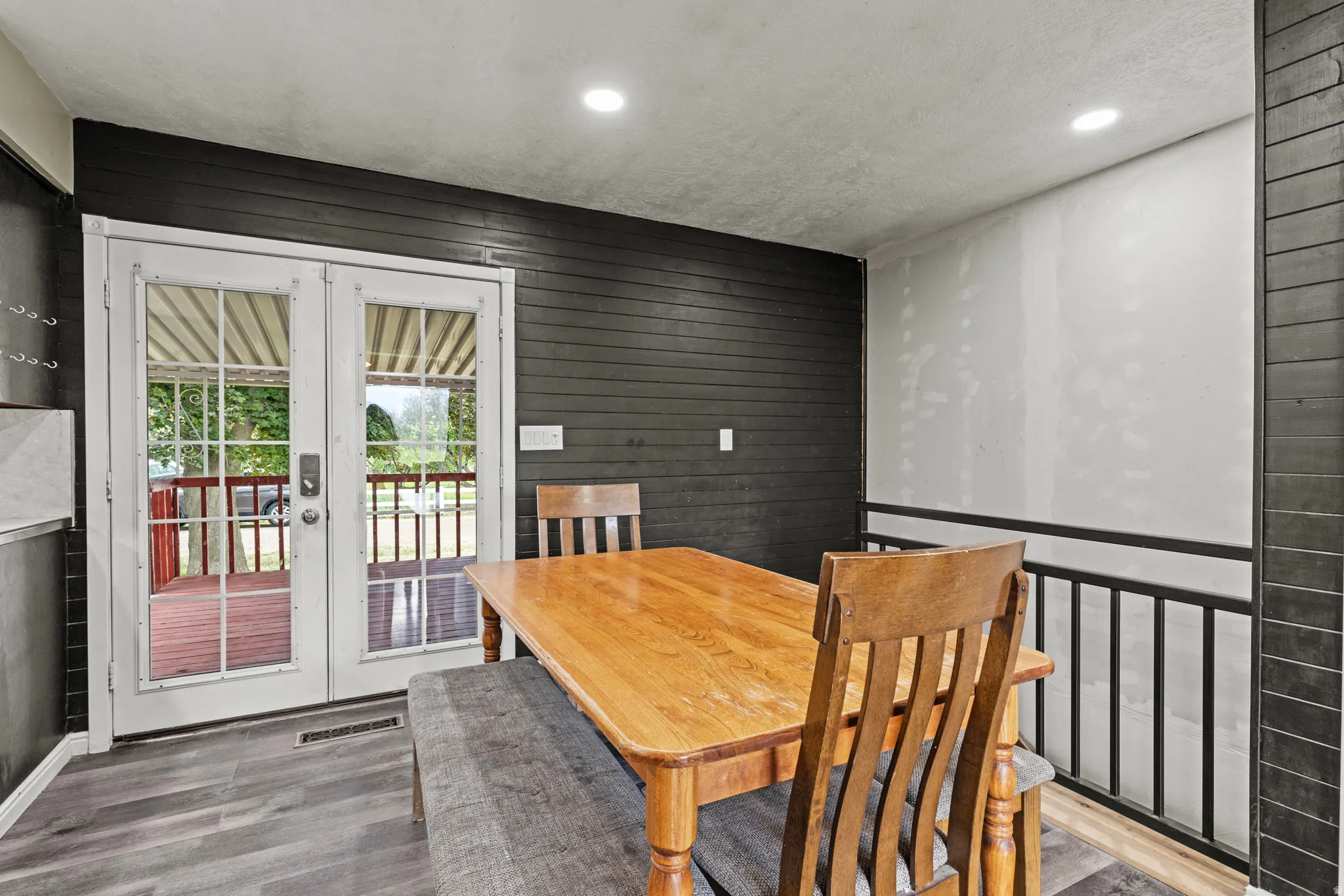 French doors opening to an outdoor deck, featuring wood-finish flooring, recessed lighting, and a black shiplap accent wall