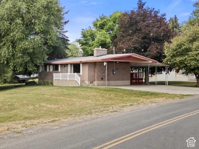 Brick residence featuring a carport with a red accent entry, an expansive grassy front yard, and mature surrounding trees