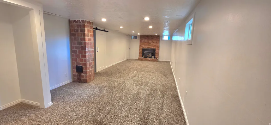 Spacious room featuring neutral carpeting, recessed lighting, and a brick fireplace