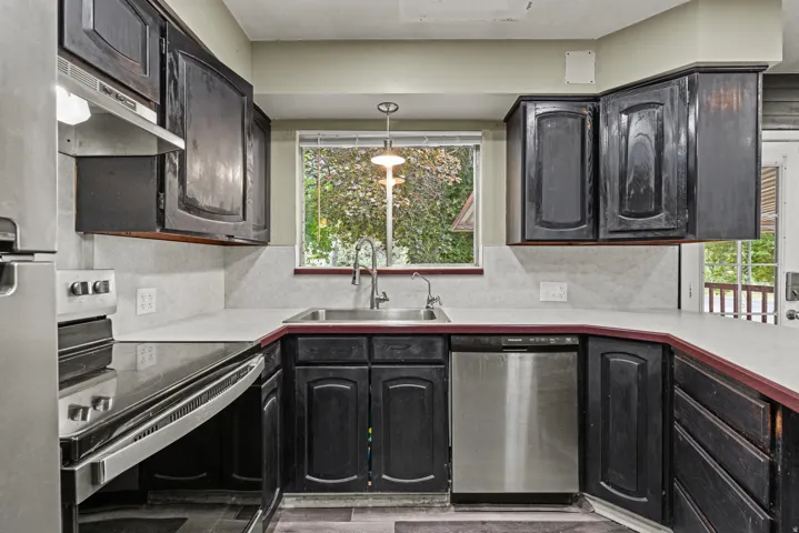 Kitchen featuring cabinetry, light countertops, stainless steel appliances, a window over the sink, and wood-finish flooring