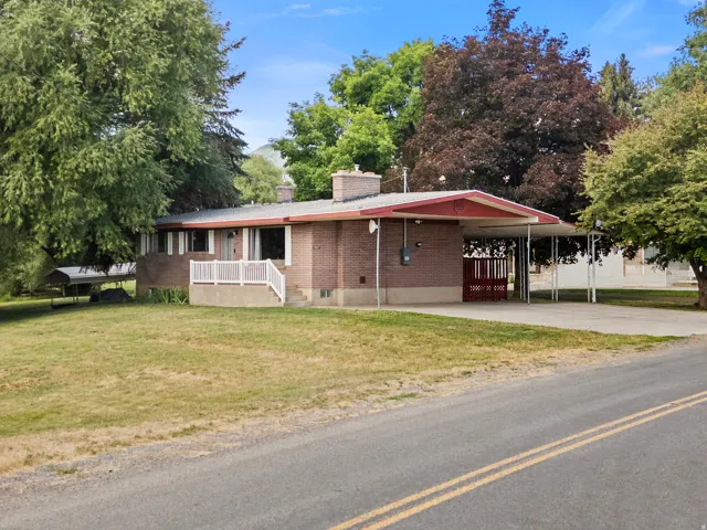 Brick residence featuring a carport with a red accent entry, an expansive grassy front yard, and mature surrounding trees