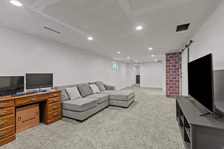 Spacious lower-level area featuring recessed lighting, a barn door, a brick chimney, and gray carpet flooring