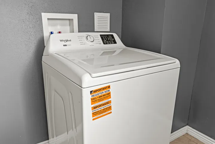 White top-loading washing machine with digital controls, featuring a water hookup box and an exhaust vent