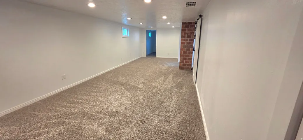 Recessed lighting illuminates neutral carpeting and a exposed brick