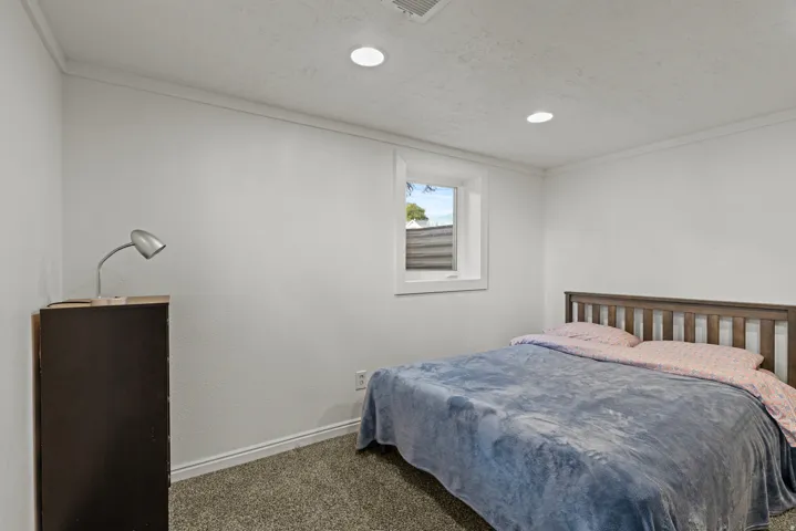 Recessed lighting illuminates a room featuring a window with white trim, and white walls.