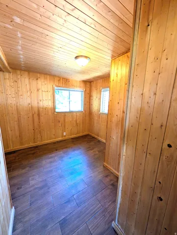 Interior room featuring wood-finish walls and ceiling, dark wood-finish flooring laid in a linear pattern, and natural light from dual windows