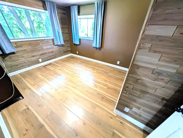 Wood-finish flooring with white trim, multiple windows, and partial wood walls