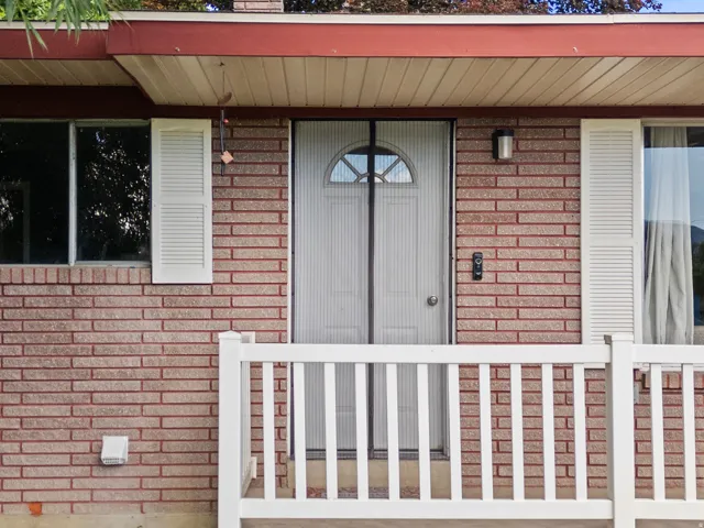 Brick facade featuring a white railing, white louvered shutters, and a white front door with an arched window