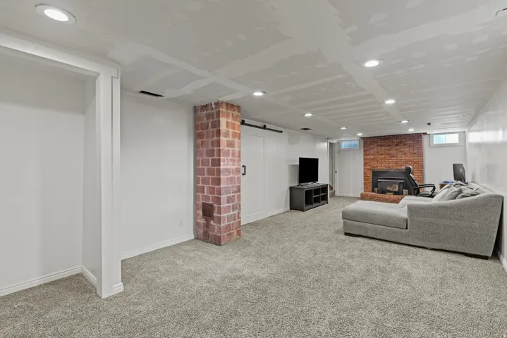 Spacious lower level featuring light gray carpeting, a prominent brick-chimney, recessed lighting, and a brick fireplace.