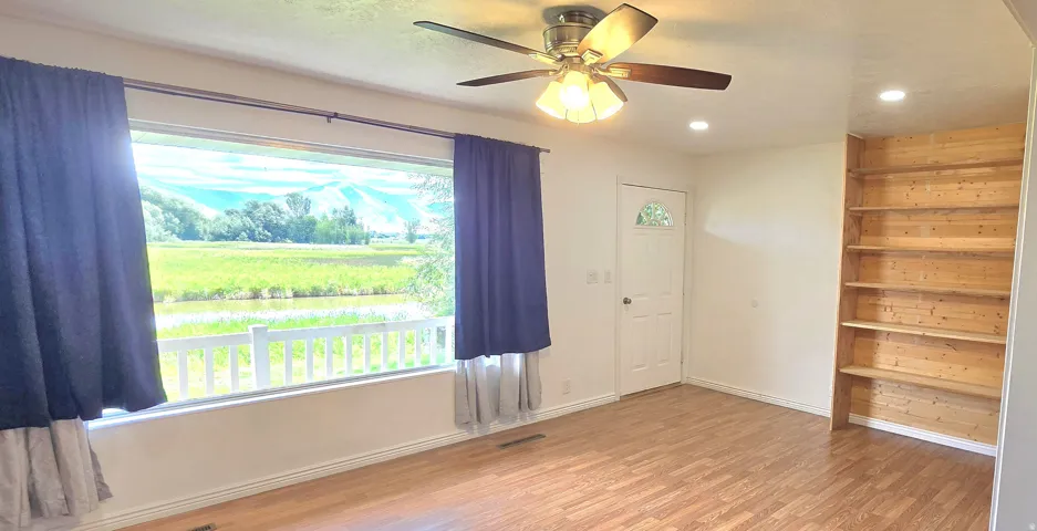Expansive window with a white railing, wood-finish flooring, built-in wooden shelving, a ceiling fan with integrated lighting, and recessed lighting