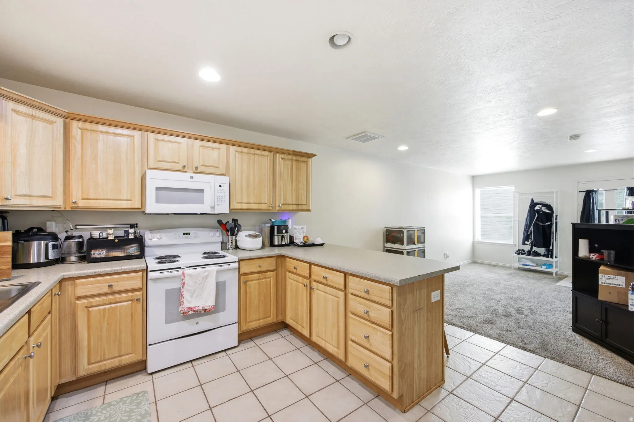 Kitchen featuring wood cabinetry, white appliances, light-toned countertops, and recessed lighting