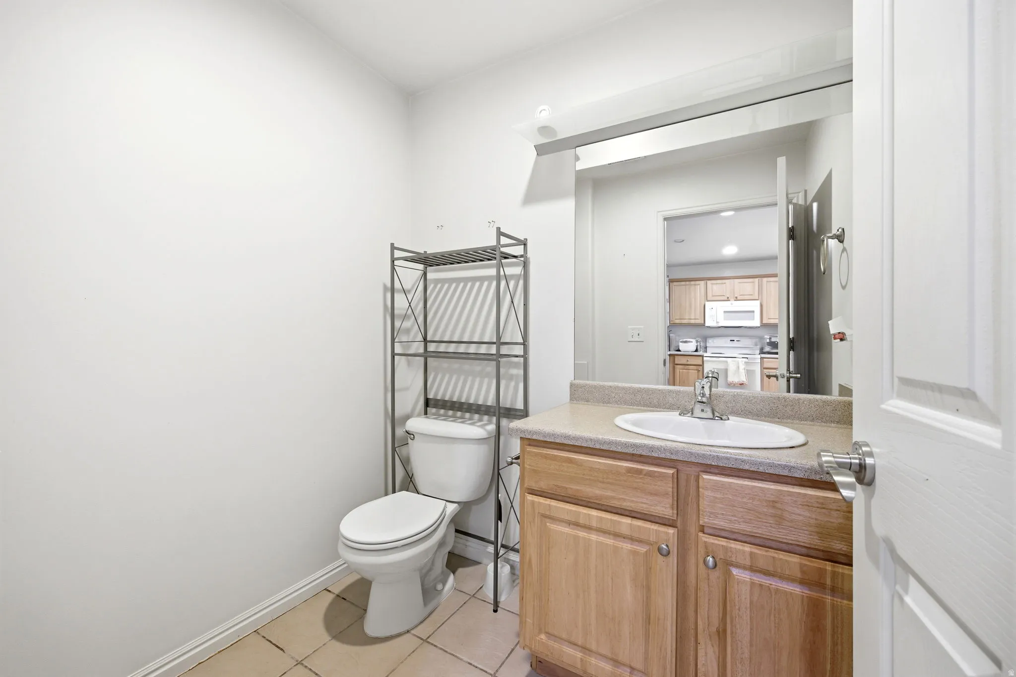 Bathroom featuring a wood-finish vanity with a built-in sink, a large wall-mounted mirror, and tile flooring