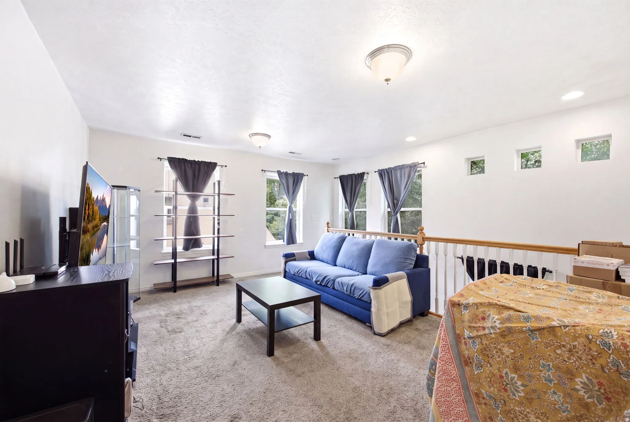Carpeted living area featuring multiple windows, a ceiling light fixture, recessed lighting, and a white baluster railing