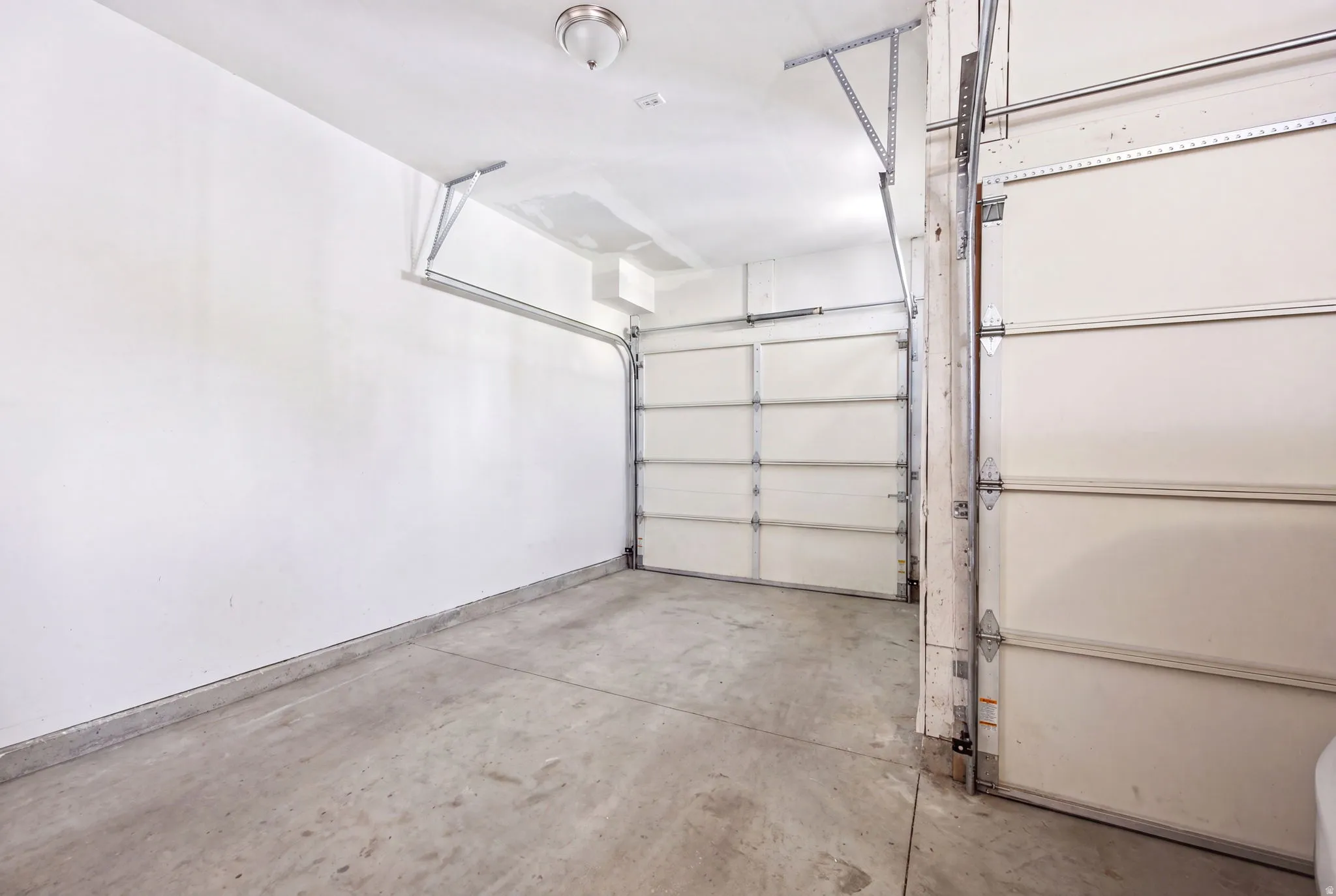 Attached two-car garage featuring a concrete floor, white walls, and overhead lighting