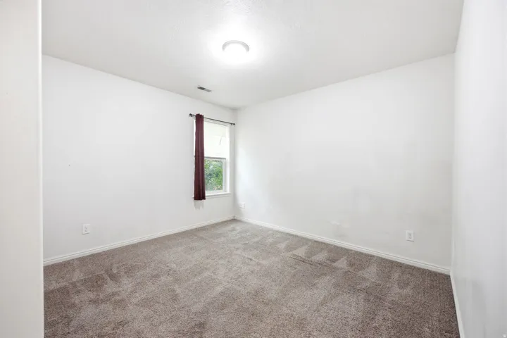 Carpeted interior space featuring white walls and a single window with dark red drapery