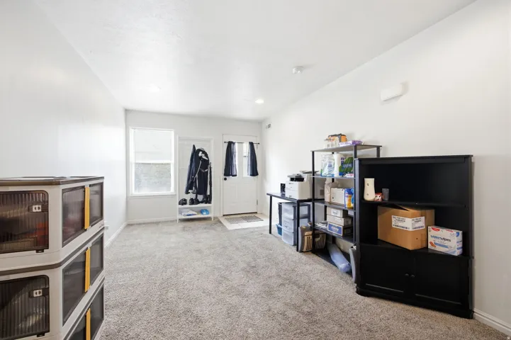 Open-concept room featuring light gray carpeting, white walls, a white entry door, and a white-framed window