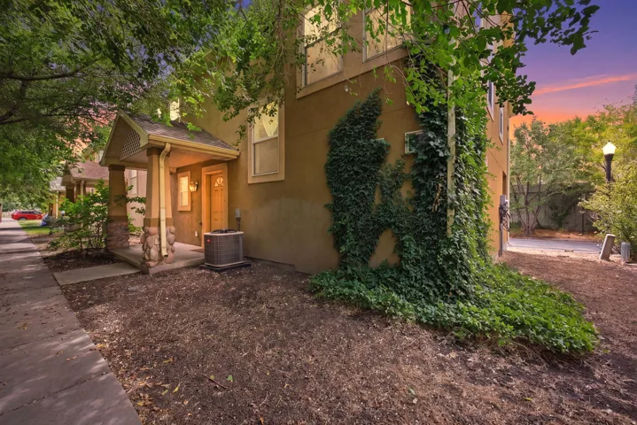 Exterior featuring a covered entry with stone-clad columns, stucco siding, and mature greenery