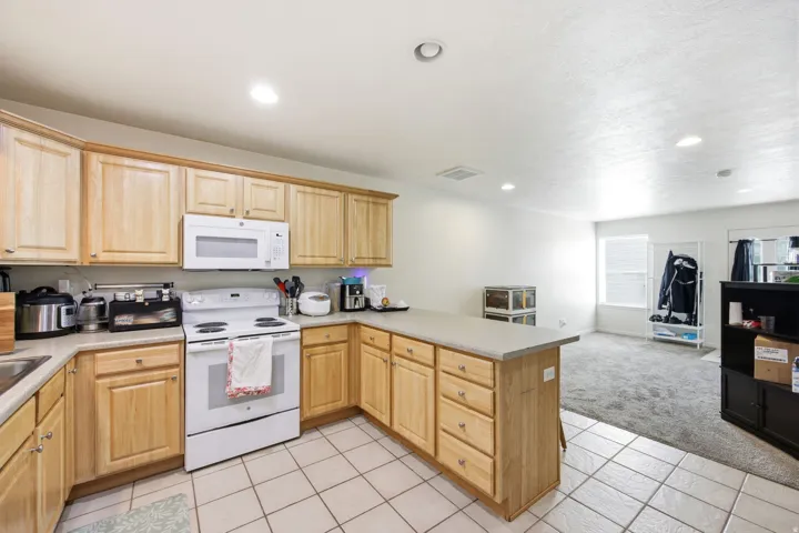 Kitchen featuring wood cabinetry, white appliances, light-toned countertops, and recessed lighting