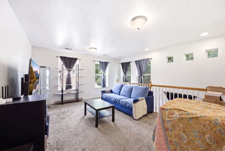 Carpeted living area featuring multiple windows, a ceiling light fixture, recessed lighting, and a white baluster railing
