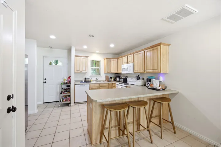 Spacious kitchen featuring light wood-finish cabinetry, a large peninsula with a countertop extension, recessed lighting, and tile flooring