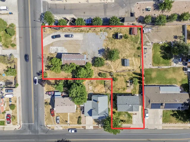 Aerial perspective showcasing two distinct parcels, one featuring a residential structure with a gray shingle roof and the other a larger lot with a gravel parking area and mature trees