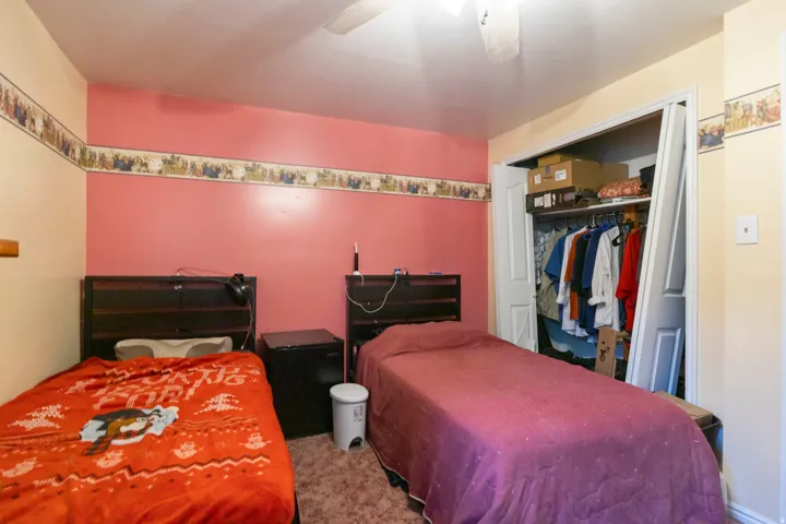 Room featuring two beds with dark wood headboards, textured carpet flooring, and a ceiling fan