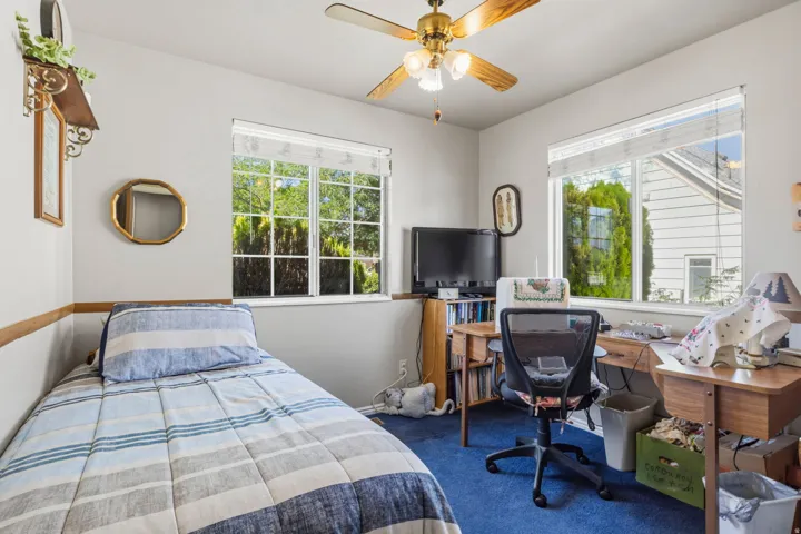 Light-filled room featuring two windows, neutral wall paint, wood-finish baseboard, and a ceiling fan with integrated lighting