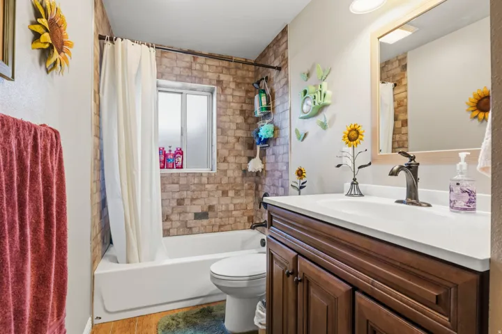 Bathroom featuring a white bathtub, tiled shower surround, frosted window, wood-finish flooring, and a dark wood vanity with a white countertop and bronze-finish faucet