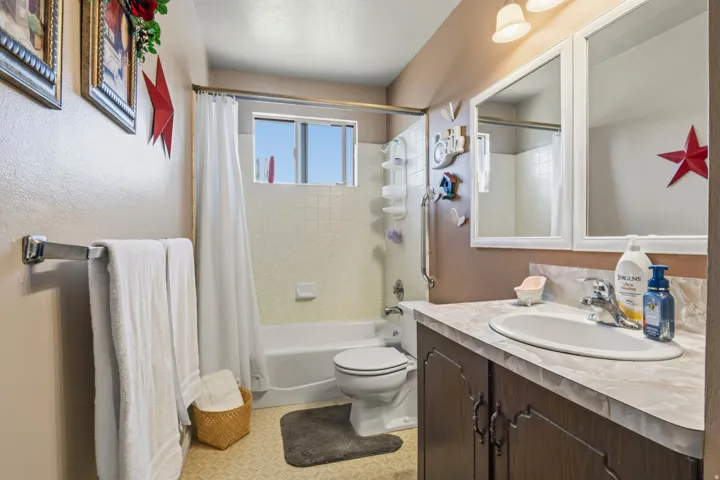 Bathroom featuring a combined tub and shower, a window providing natural light, a single vanity with storage, and decorative wall mirrors