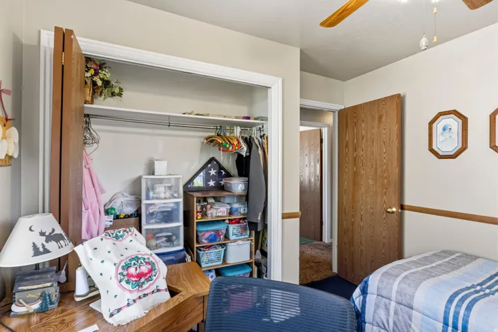 Bedroom featuring a built-in closet with bi-fold doors, overhead ceiling fan, and two-tone wall treatment with a wood-finish chair rail