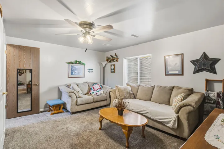 Spacious interior featuring a ceiling fan with integrated lighting, window with blinds, wood-finish flooring, and light-toned walls