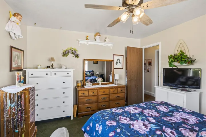 Ceiling fan with integrated lighting, neutral wall paint, wood-finish interior door, and green carpeting