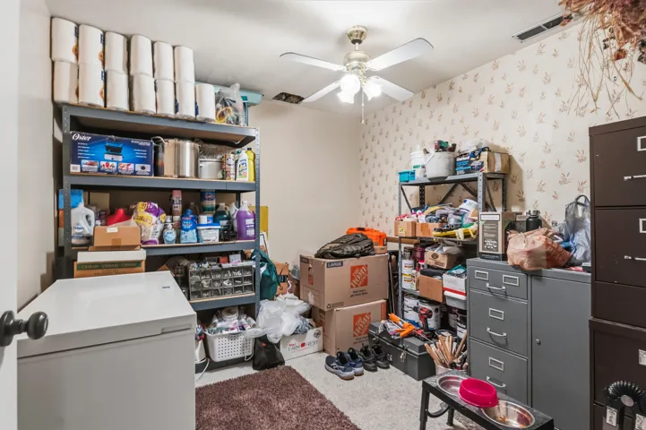Utility room featuring a ceiling fan with integrated lighting, wall-mounted shelving units, and a textured wallpaper accent wall