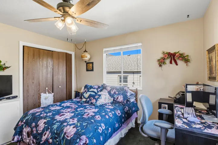 Bright room featuring a window with natural light, a ceiling fan with integrated lighting, wood-finish bi-fold closet doors, and carpet flooring