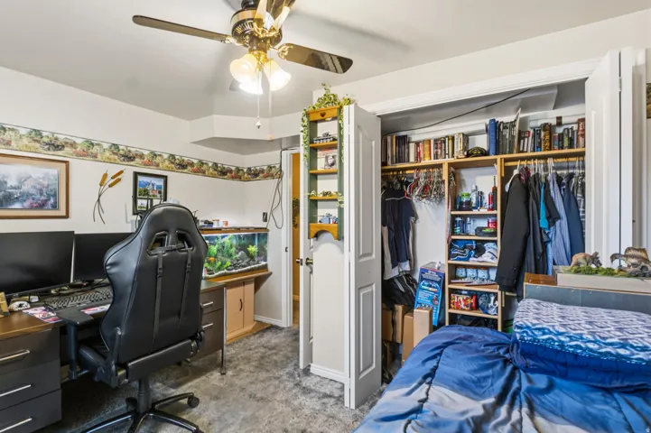 Bedroom featuring a ceiling fan with integrated lighting, built-in closet organization with shelving and hanging rods, a dedicated desk area, and wall-to-wall carpeting