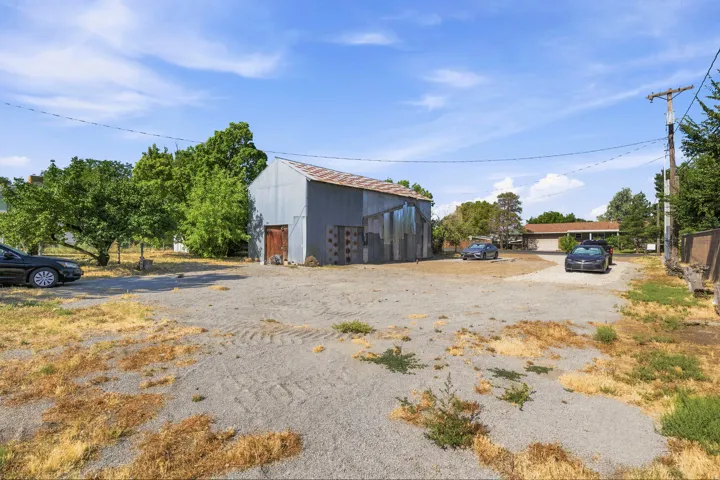 Gravel lot featuring a corrugated metal outbuilding with a wood door, surrounded by mature trees