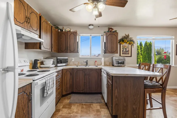Kitchen featuring wood-finish cabinetry, white appliances, and a peninsula with seating